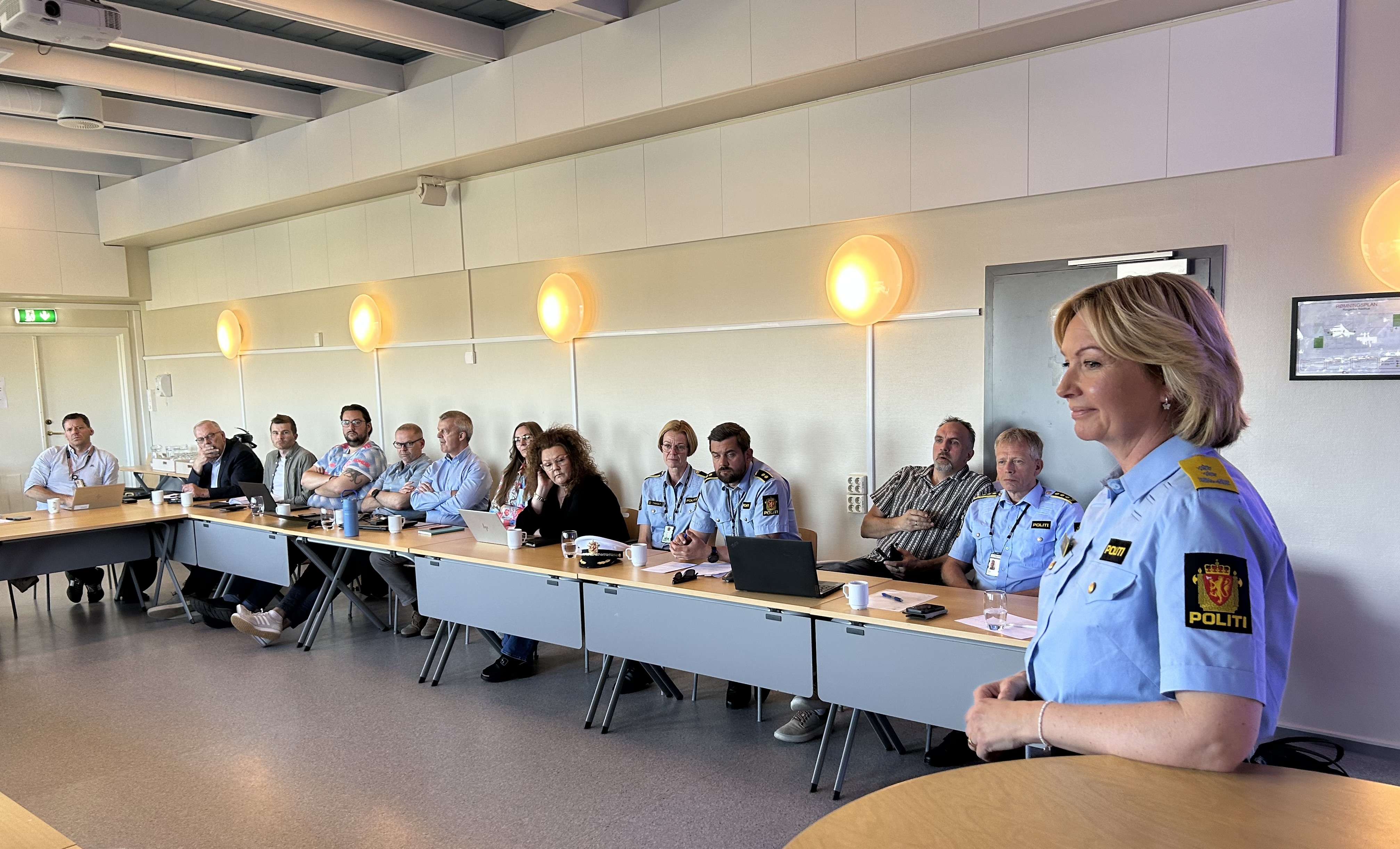 Bildet er tatt i politirådet. Vi ser politismesteren stå foran de andre inne i salen. Det er mange tilhørere.
