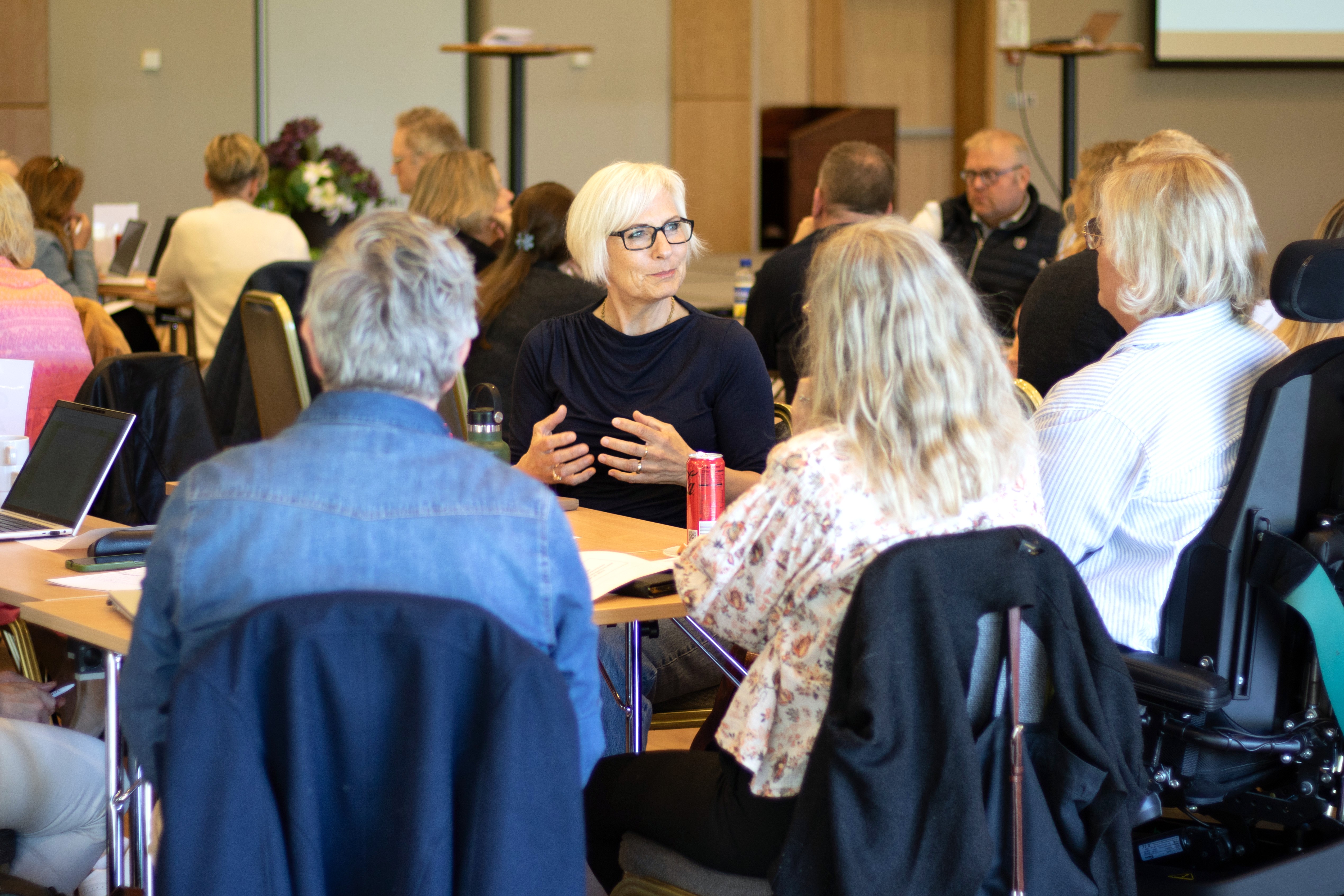 Bildet viser ei dame som er en del av et gruppearbeid rundt et bord.